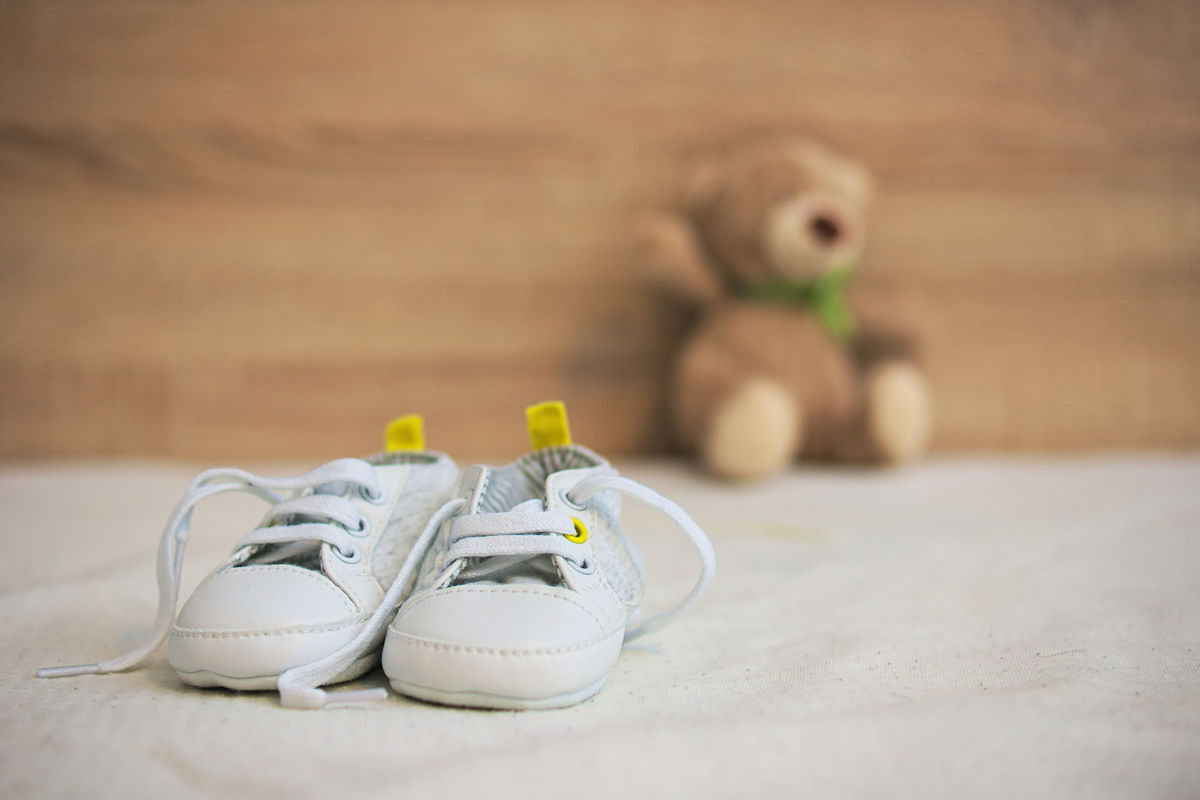 A pair of baby shoes with a soft-focus teddy bear in the background.