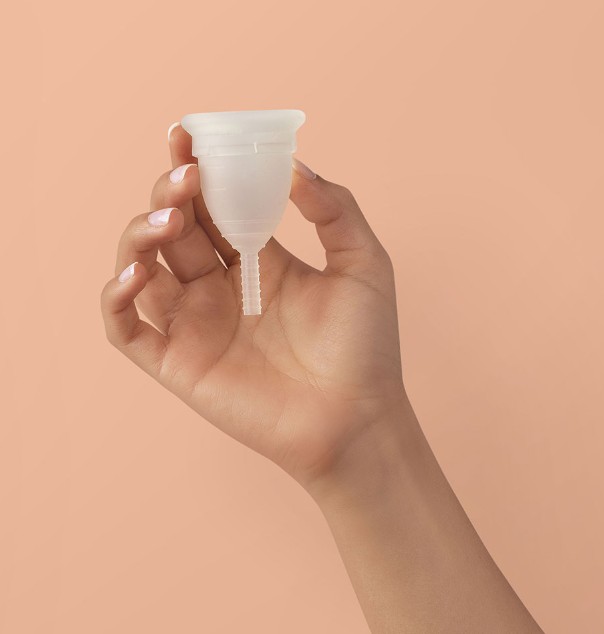 A clear reusable menstrual cup held in one hand